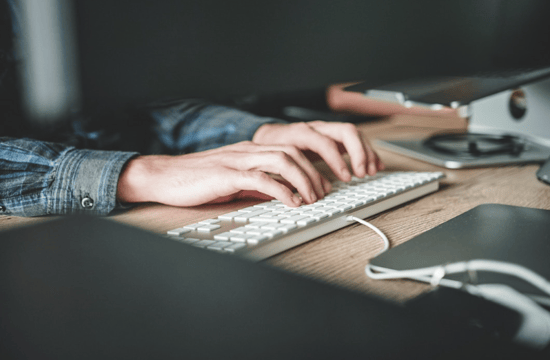 Individual typing on a keyboard at a desk, highlighting automation and scheduling tools for improved communication efficiency.