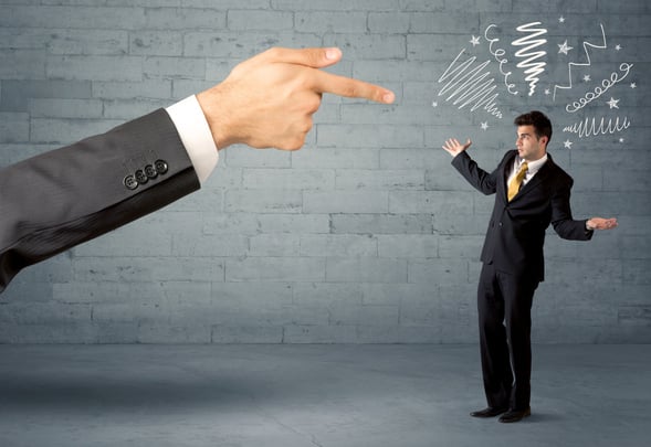 Boss firing employee concept with a huge hand pointing at confused business person illustrated by drawn lines in front of grey brick wall
